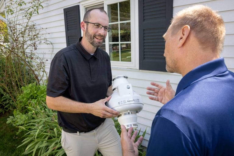 Two men discussing a radon mitigation system outside of a home.
