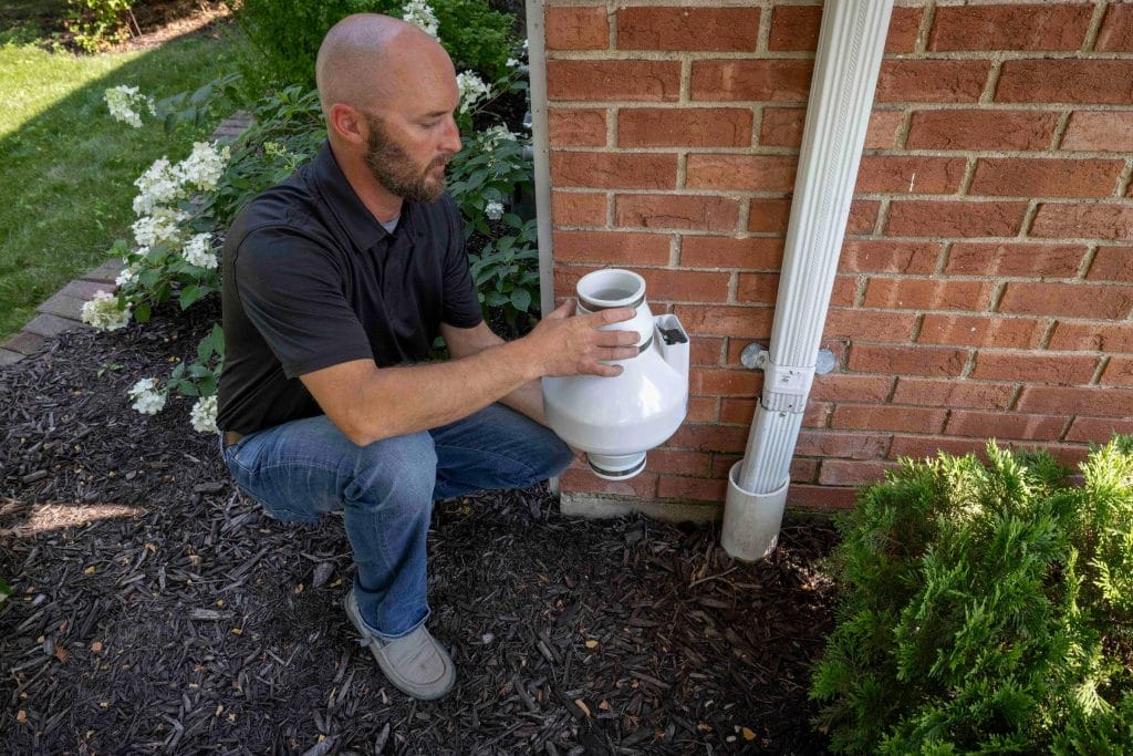A man putting in a radon mitigation system on someone's home exterior.