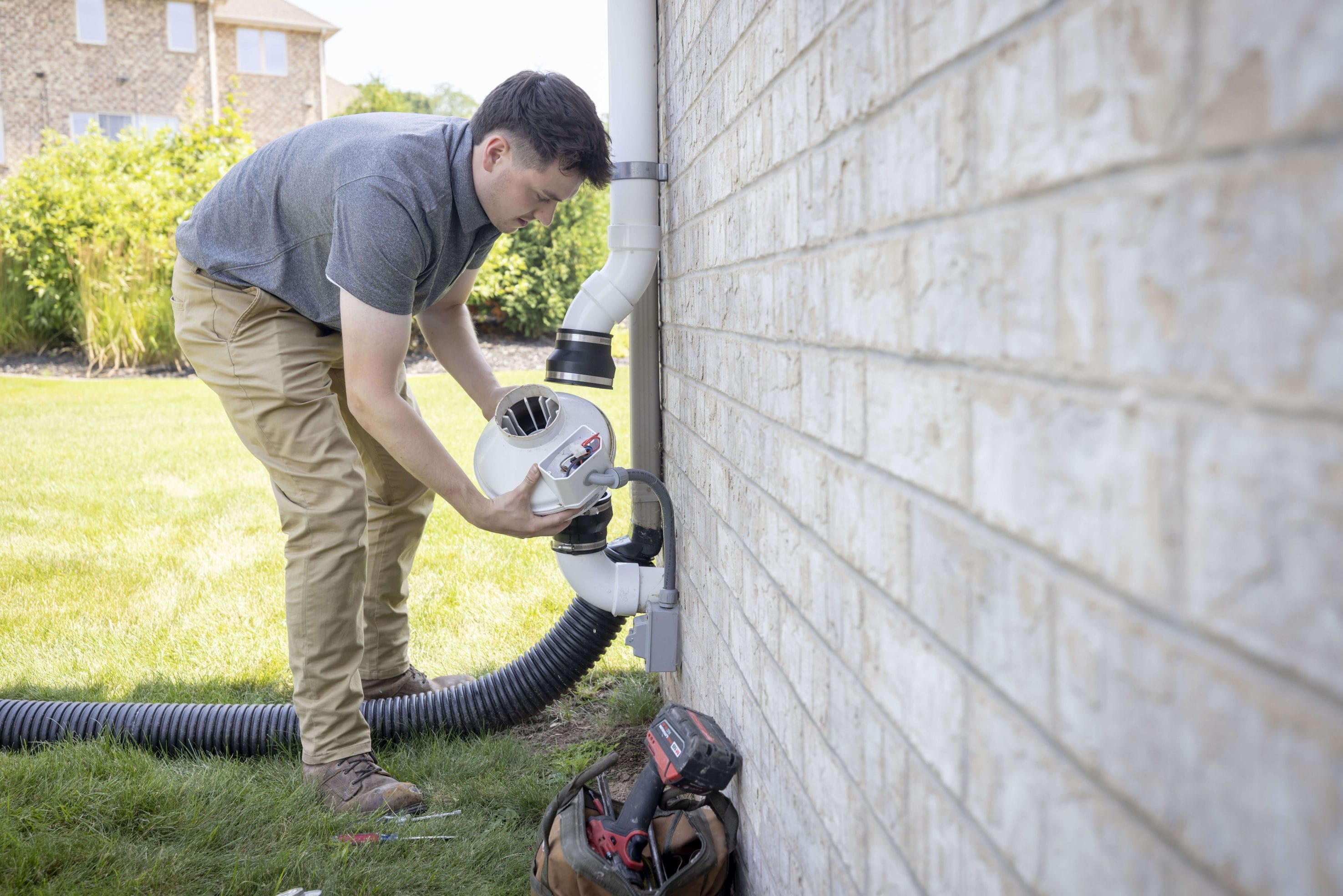 A man adjusting a radon mitigation system in someone's home exterior.