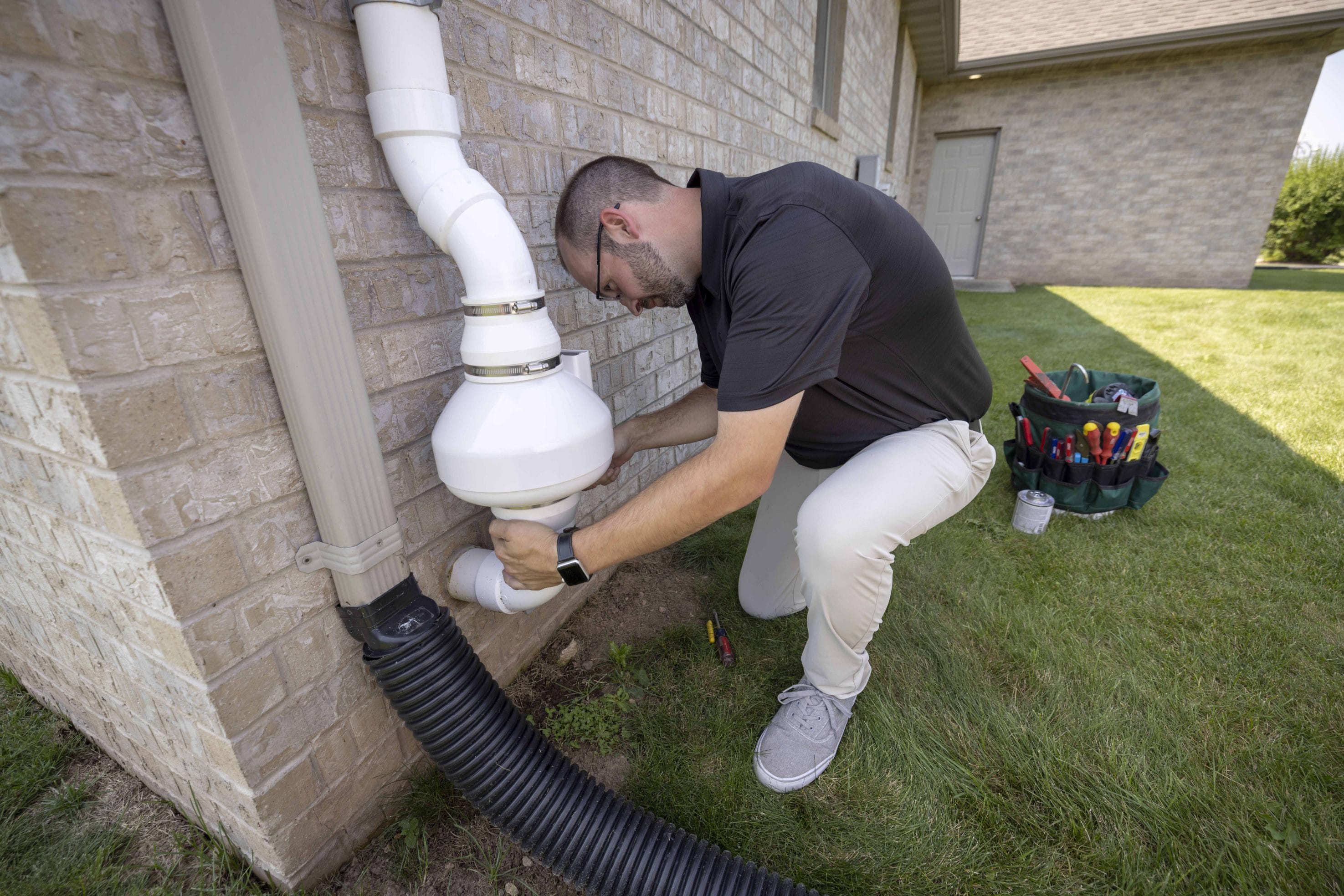 A man adjusting a radon mitigation system in someone's home exterior.