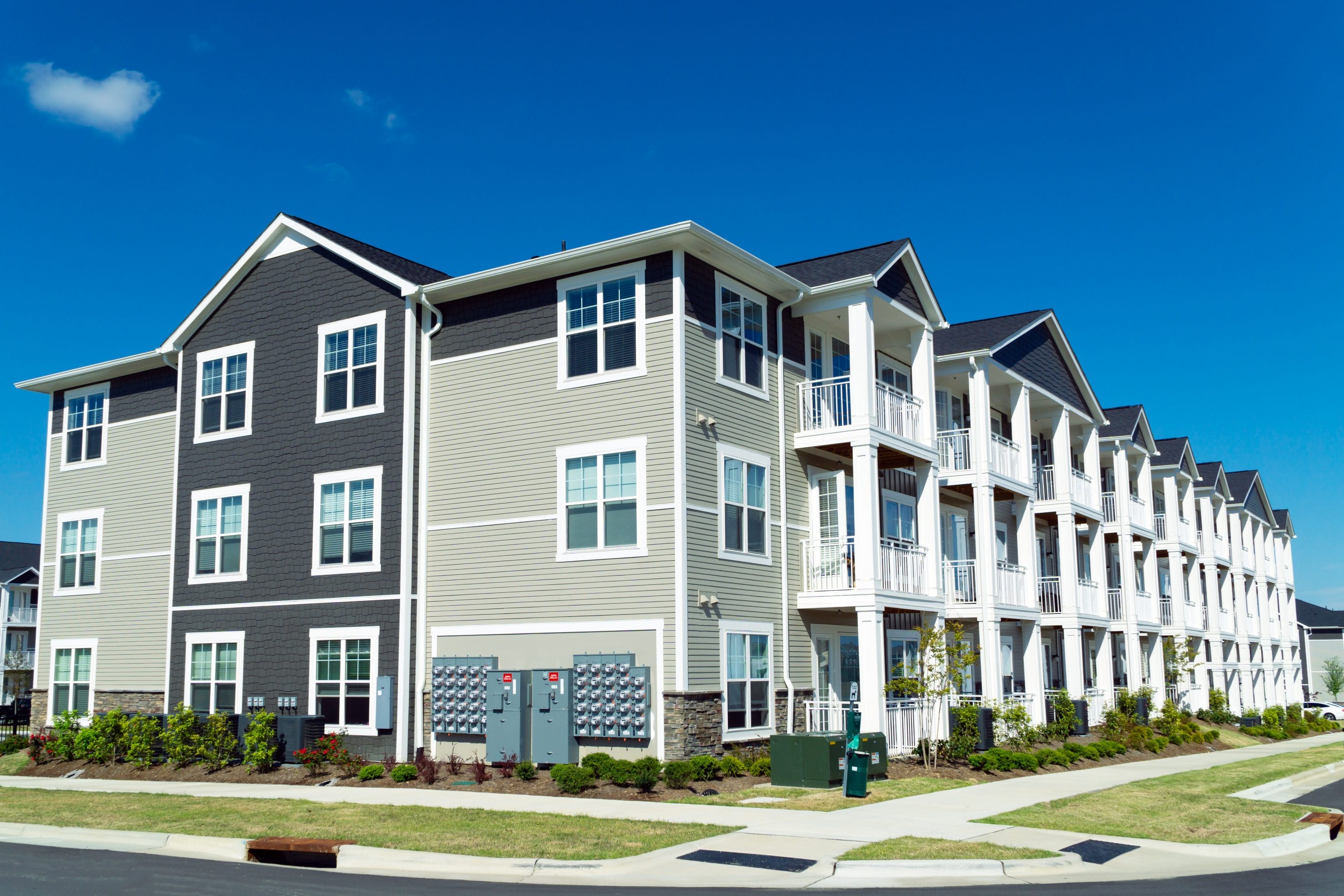 An exterior picture of apartment buildings with trees and bushes out front.