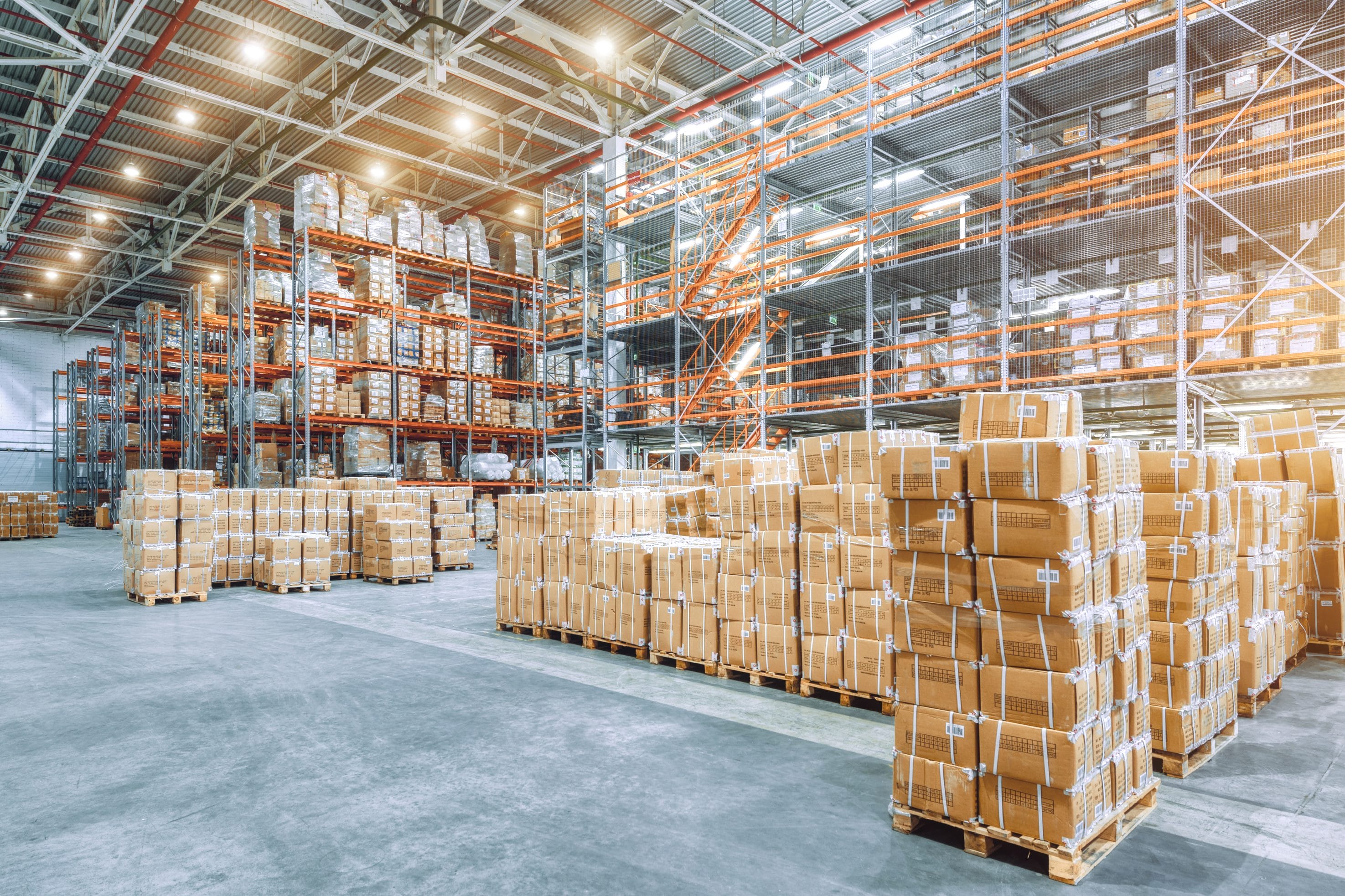 An open warehouse with many boxes, shelves, and pallets throughout it.