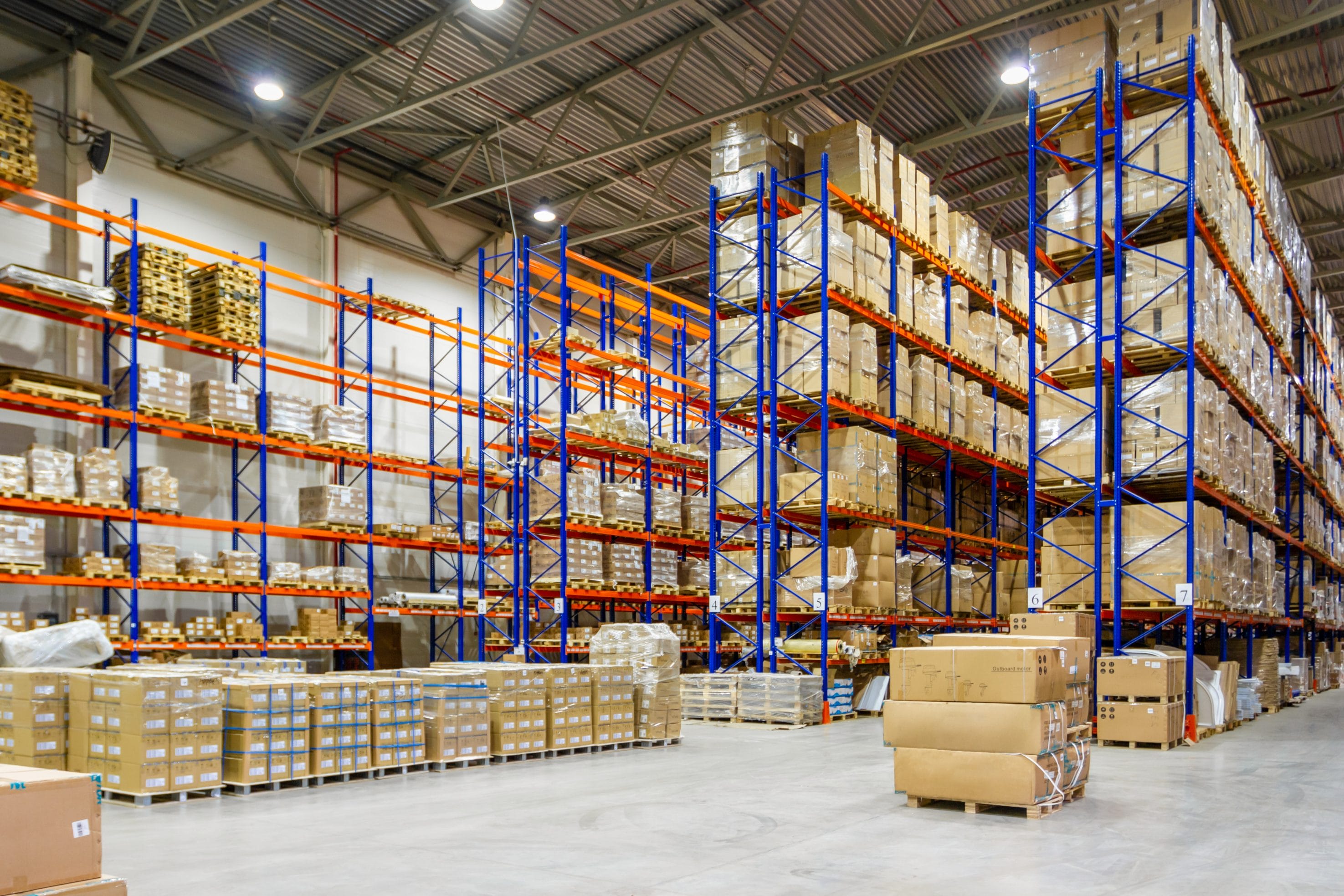 An open warehouse with many boxes, shelves, and pallets throughout it.