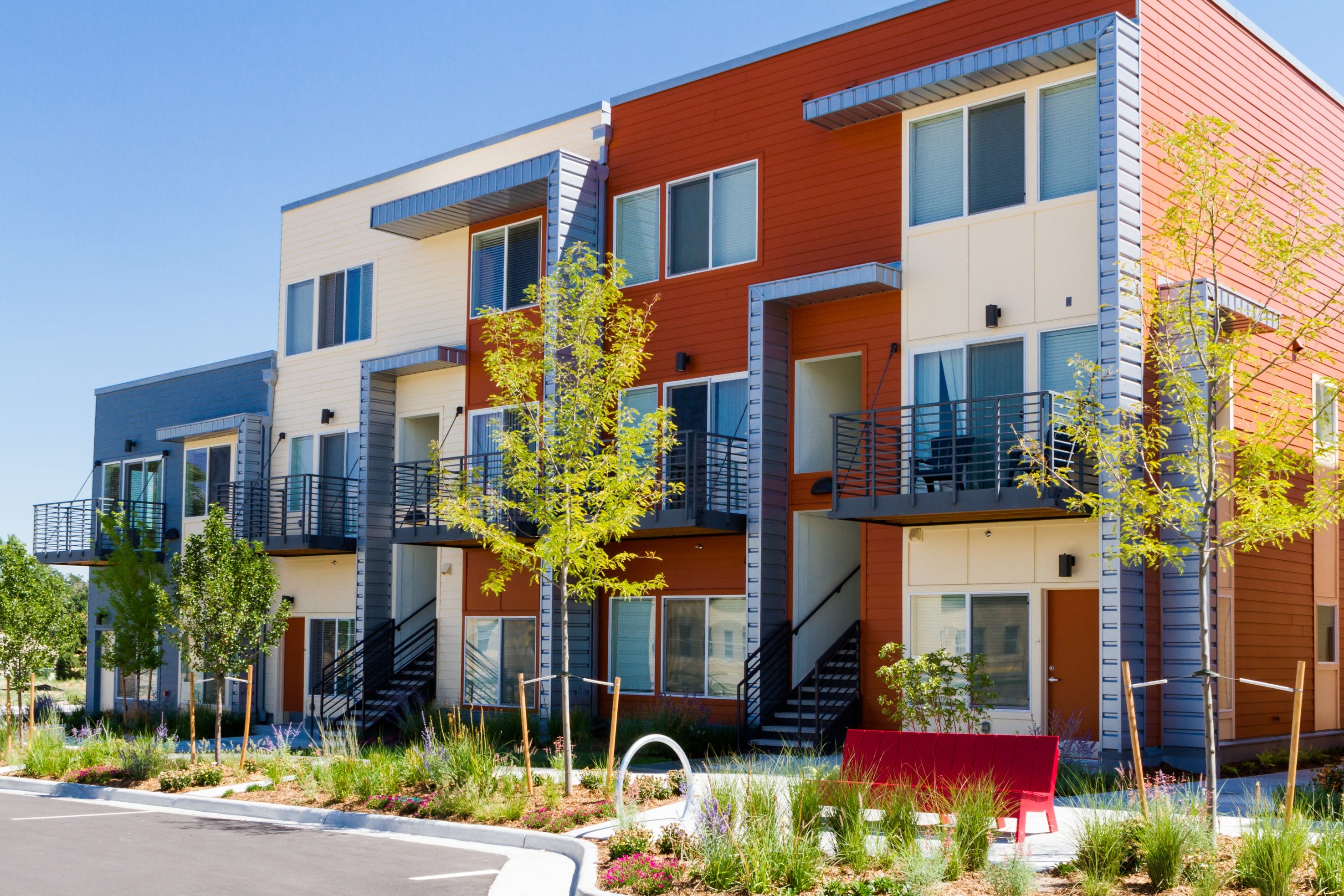 An exterior picture of apartment buildings with trees and bushes out front.