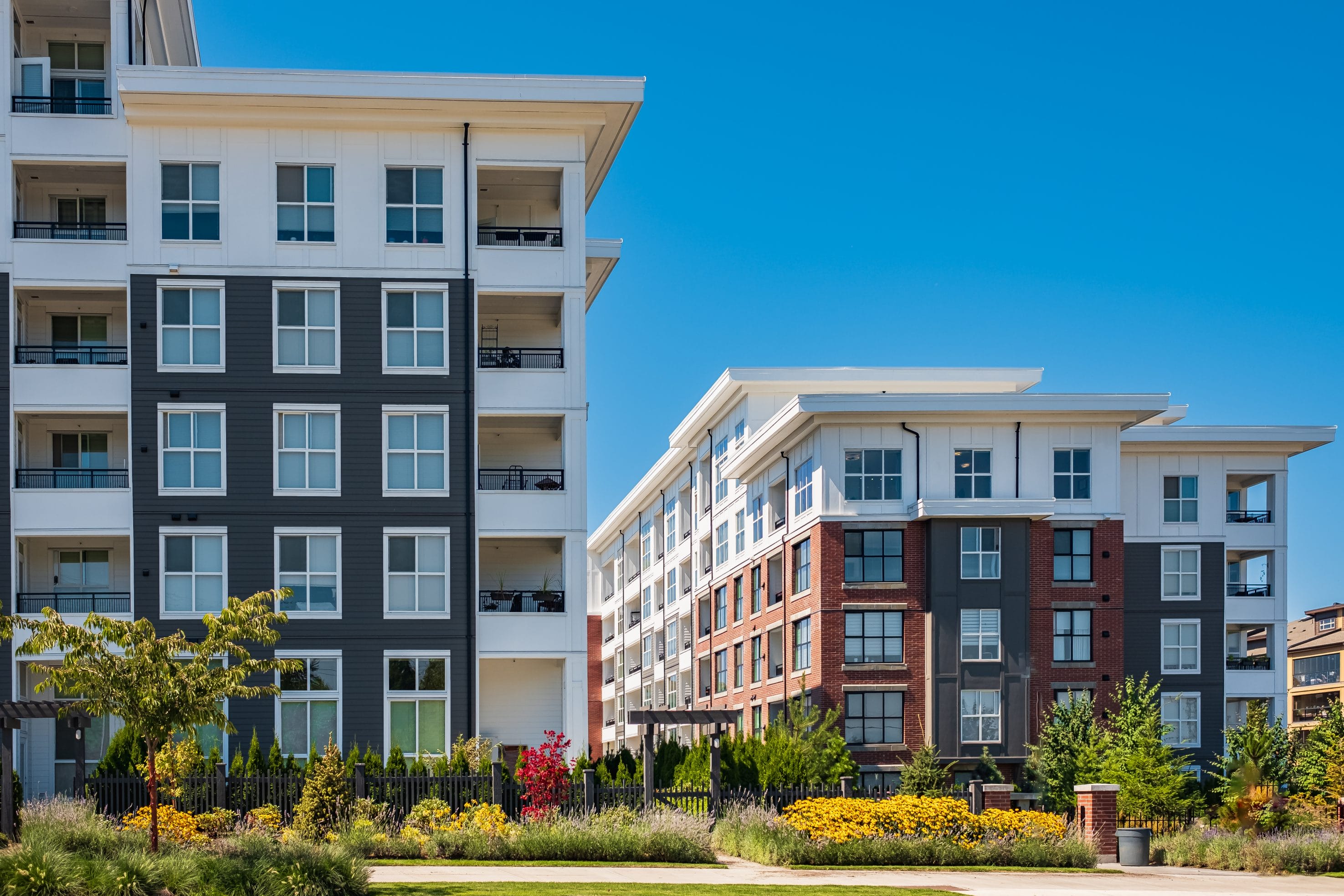 An exterior picture of apartment buildings with trees and bushes out front.